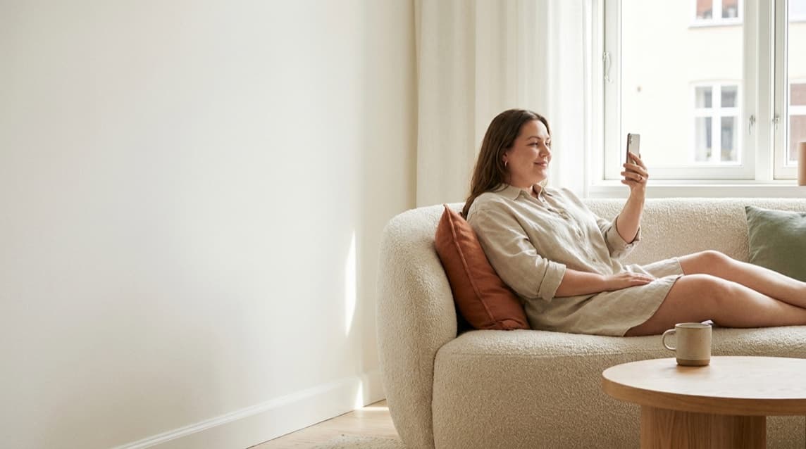 Photo of a woman sitting on the sofa at home, in a video consultation on her phone